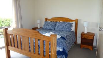 Quarto com cama de madeira, duas mesas de cabeceira e janela com cortinas.