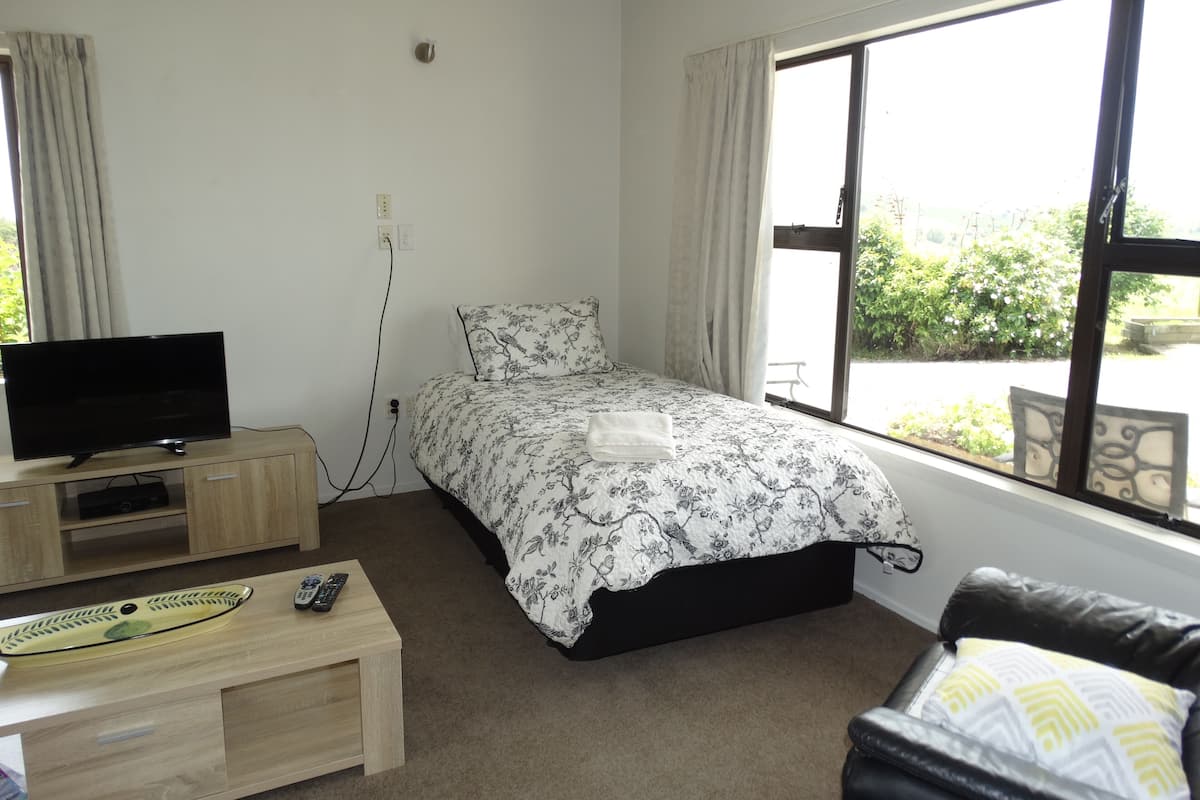 Um quarto com uma cama, televisão, escrivaninha e janela.