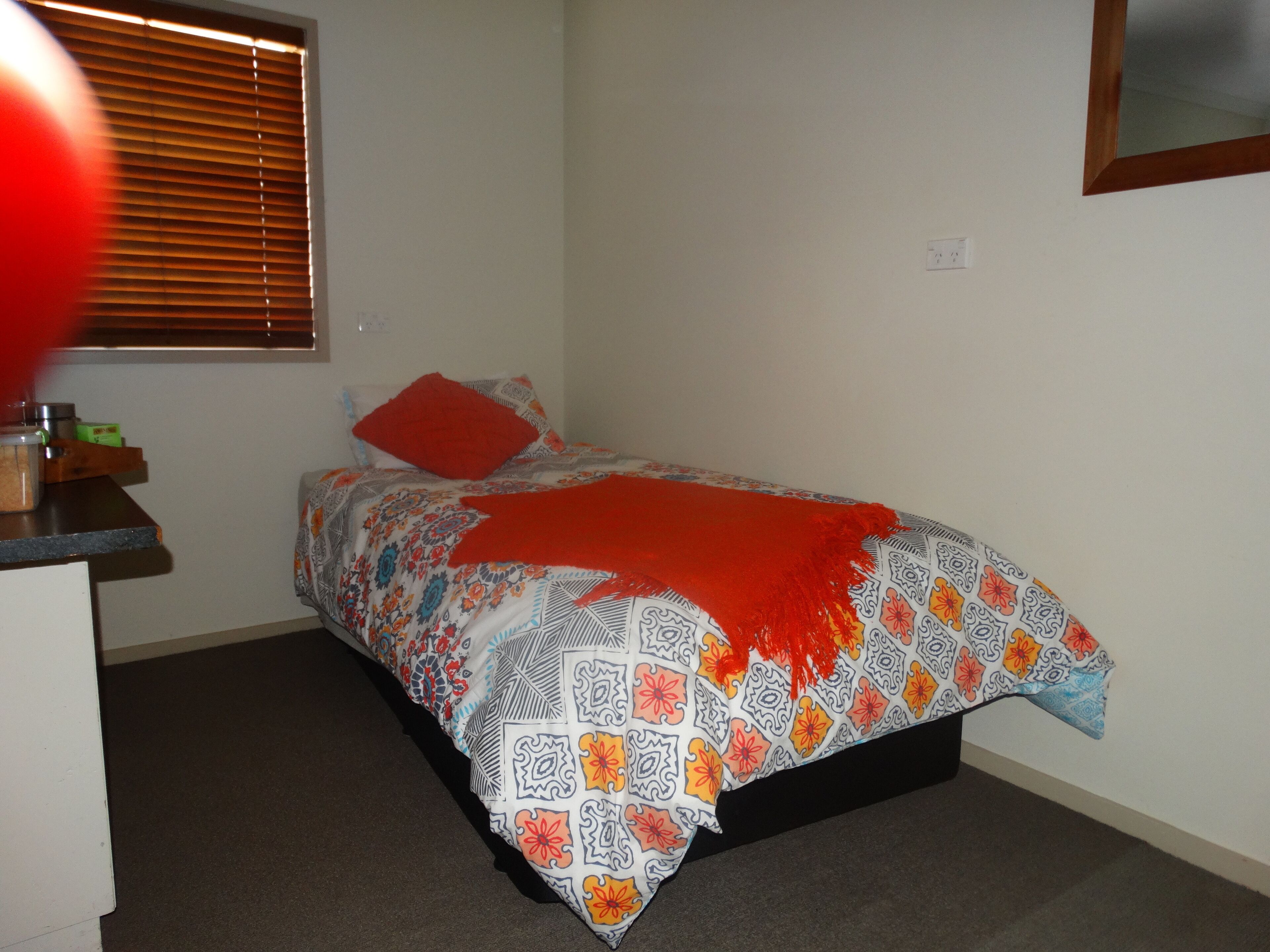 A small, neatly arranged bedroom with a bed, a nightstand, and a window with blinds.