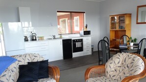 A modern kitchen with white cabinets, a black dishwasher, and a microwave. There is a dining area with wicker chairs and a wooden cabinet.