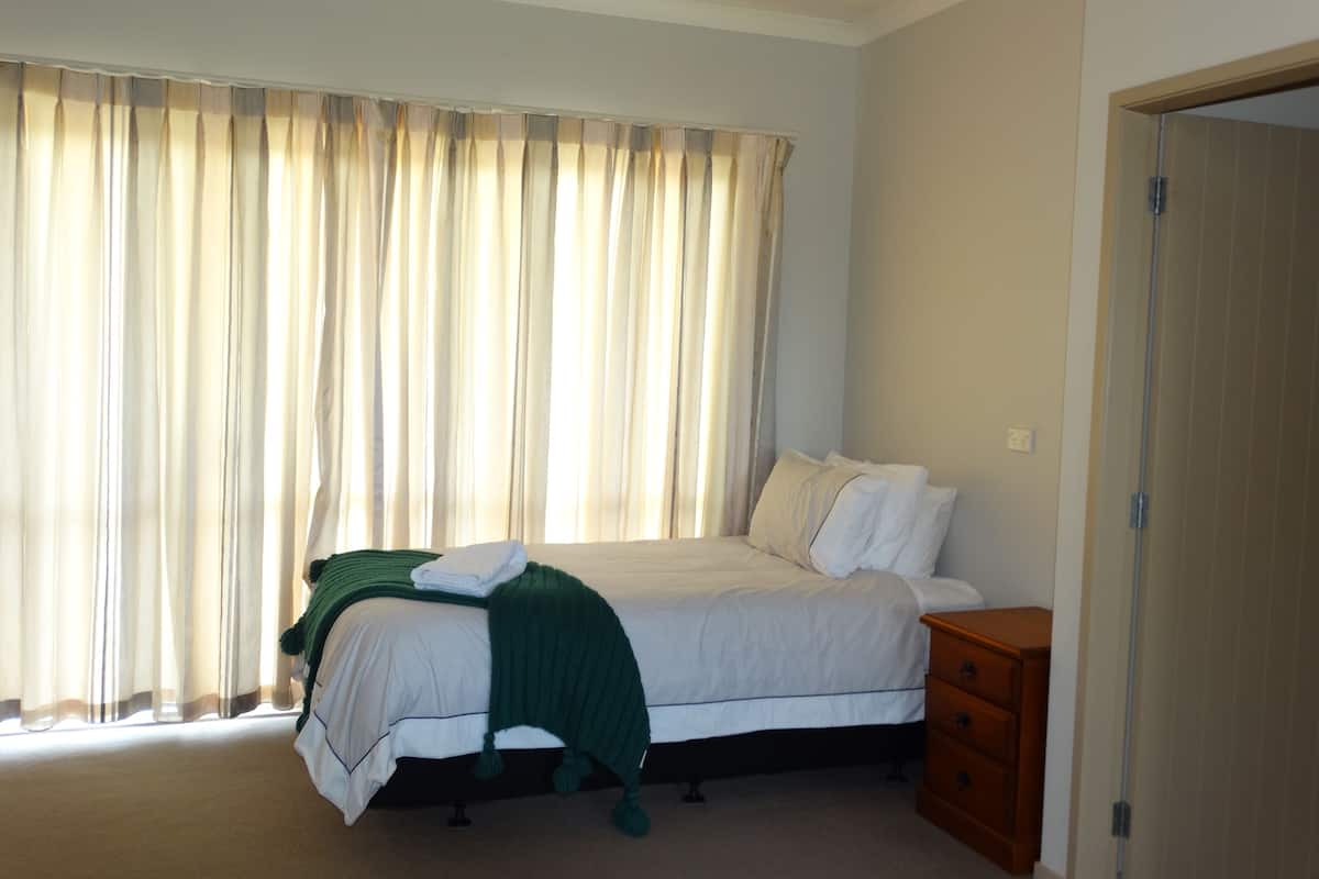 Quarto com uma cama, mesa de cabeceira e cómoda de madeira.