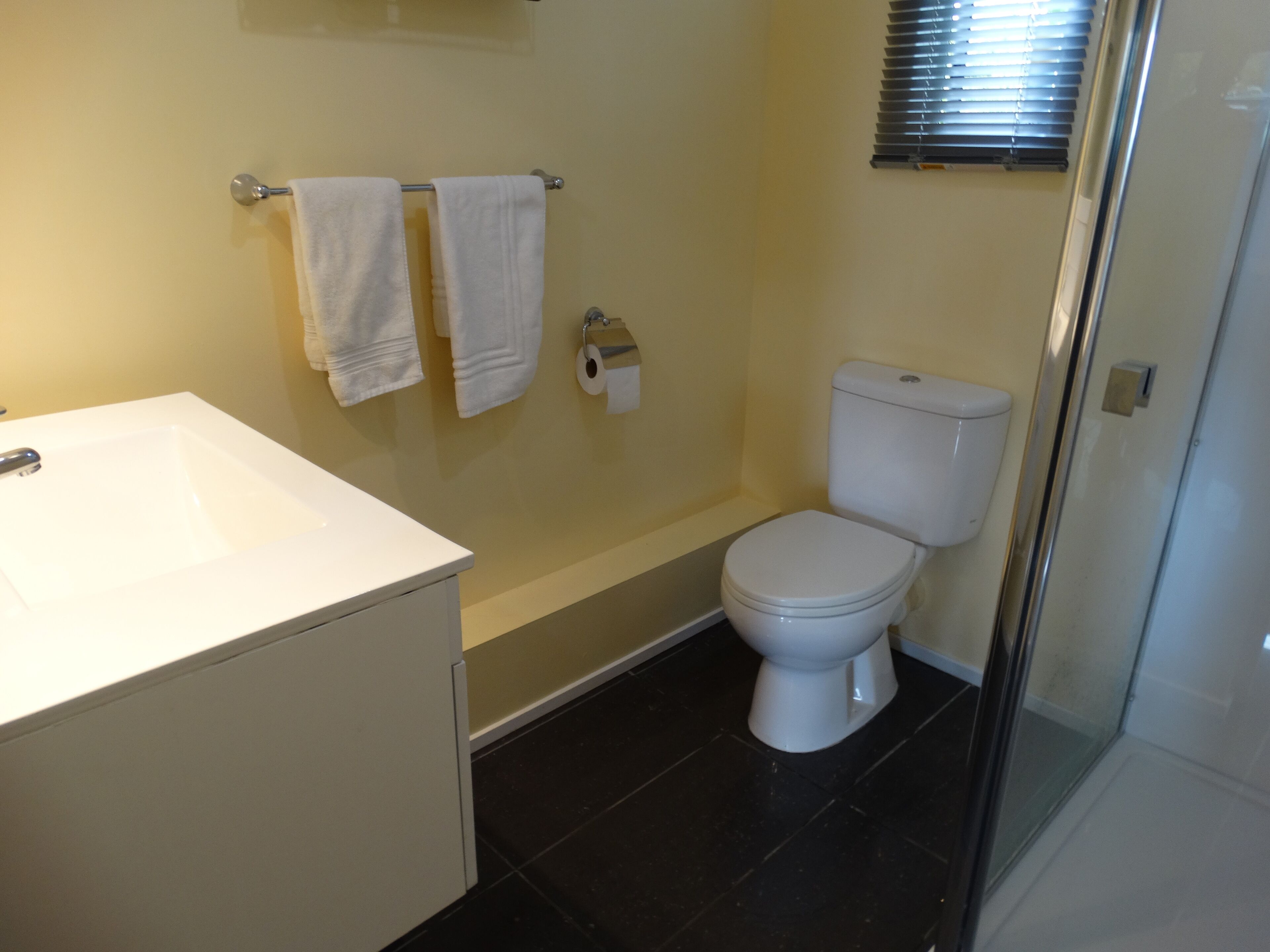 A bathroom with a white sink, two towels on a rack, a toilet, and a glass shower enclosure.