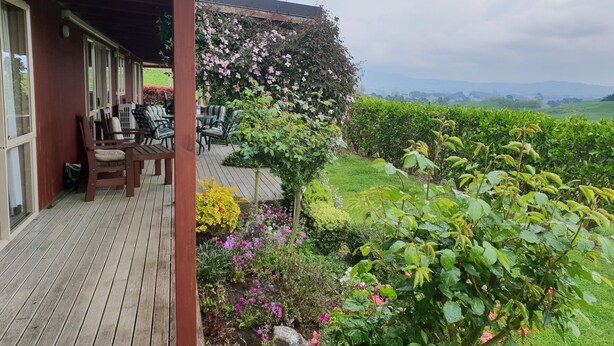 A wooden deck with outdoor furniture, surrounded by lush greenery and flowering plants.
