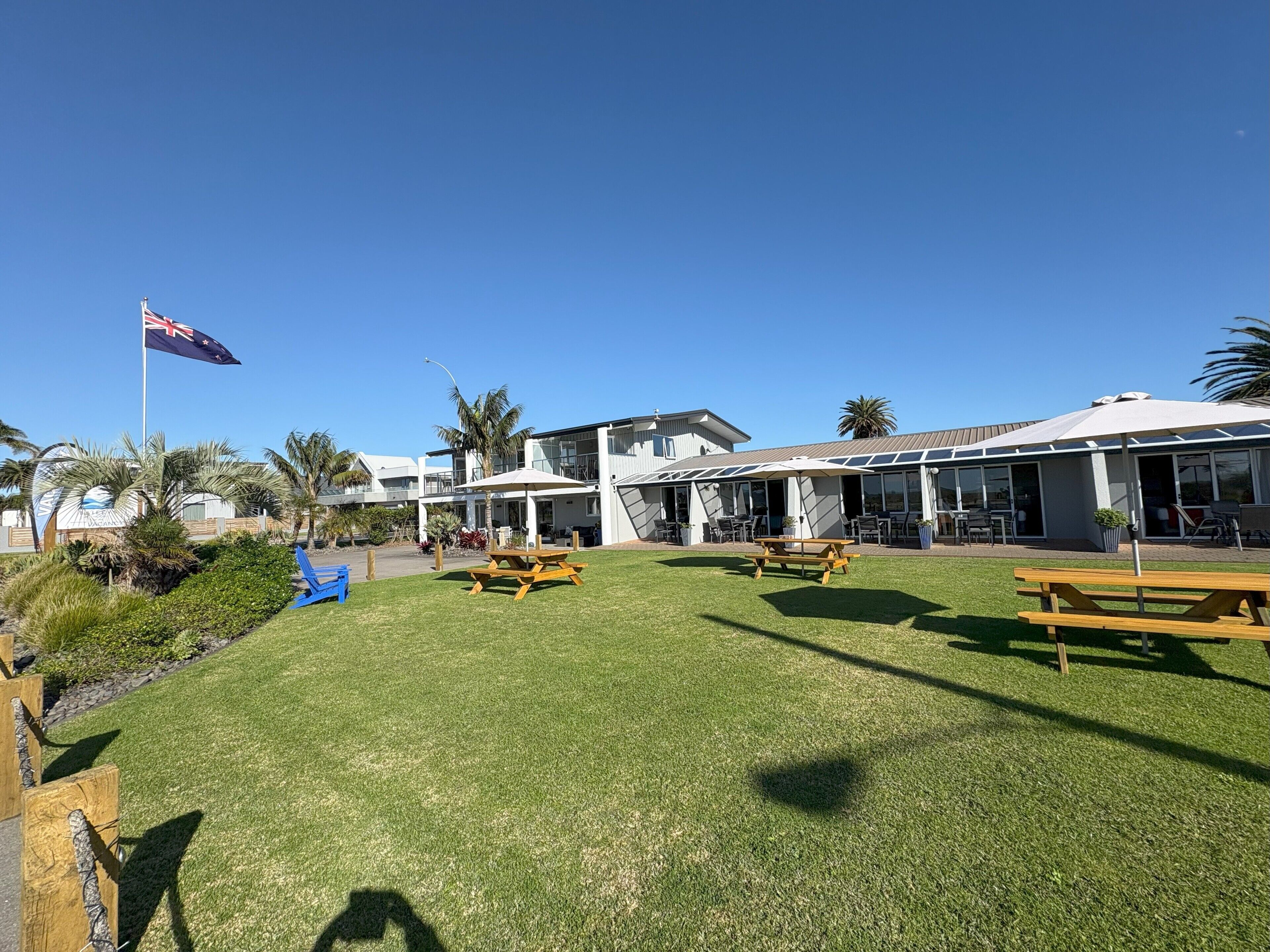 Een hotel met terras, een vlag en palmbomen.
