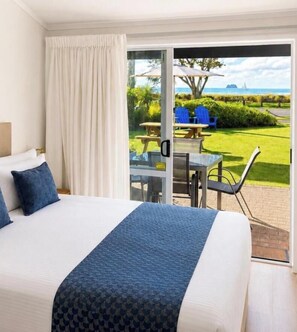 A hotel room with a bed, a view of the outdoors, and a patio area with chairs and a table. - Bailey's At The Beach Motel (Whitianga)