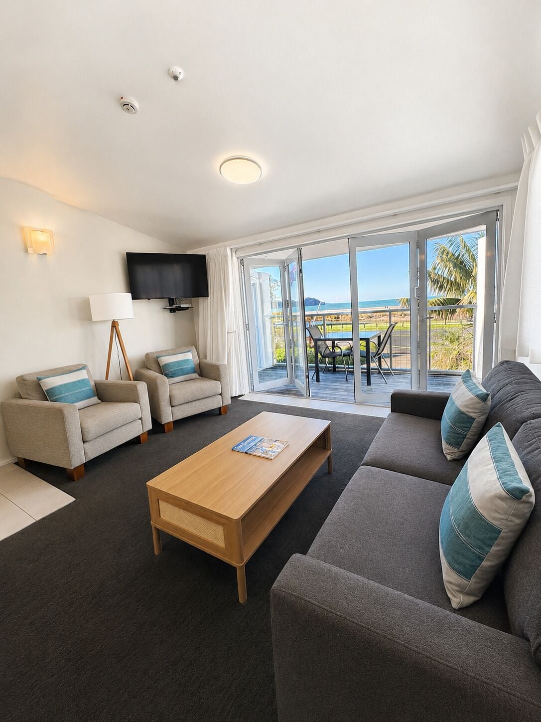 A modern living room with a sofa, armchairs, a coffee table, a TV, and a balcony with a view.