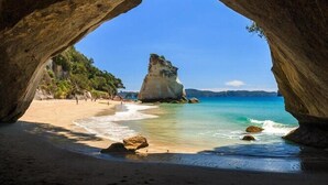 Eine Strandansicht, eingefasst von einem natürlichen Felsbogen, mit klarem türkisblauem Wasser und einer markanten Felsformation.