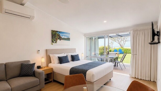 Ein Hotelzimmer mit Bett, einer Couch, einem Esstisch mit Stühlen, einem Fernseher und einem Balkon mit Blick.