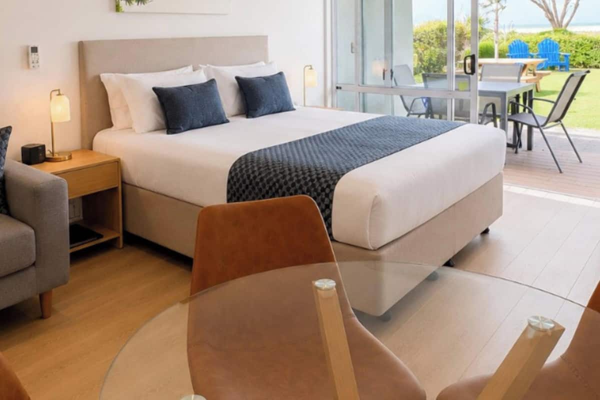 A modern hotel room with a bed, a glass table, and a view of the outdoors.