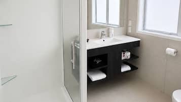 A modern bathroom with a glass shower enclosure, a white sink, a dark vanity, and a window providing natural light.