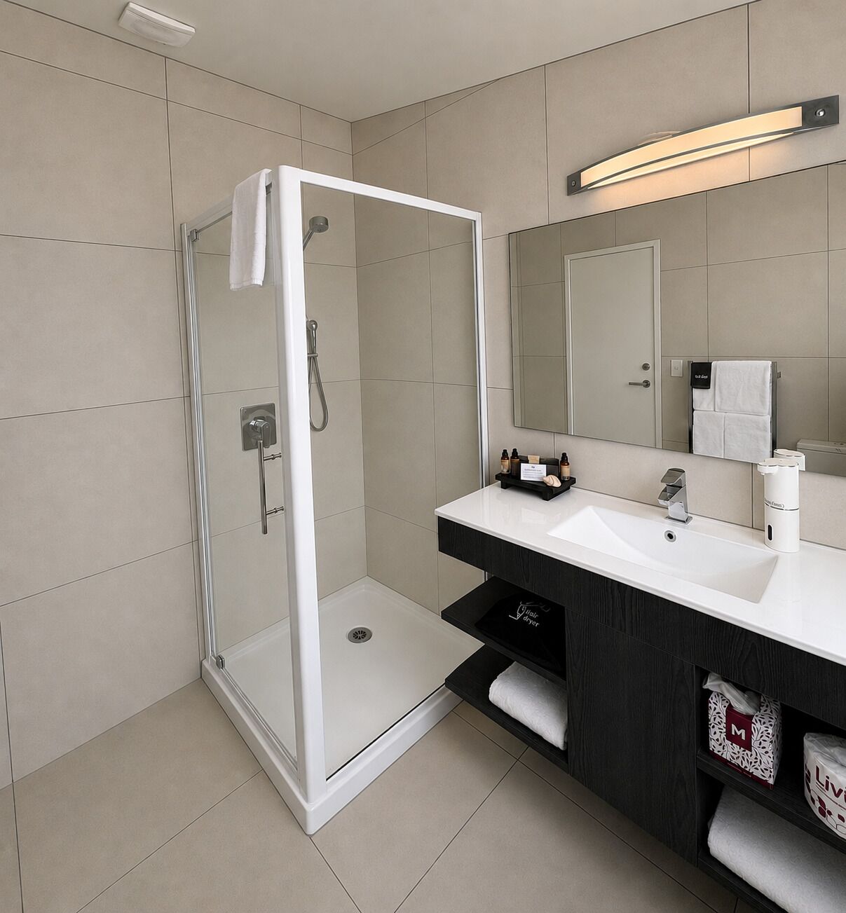 Un baño moderno con ducha acristalada, lavamanos blanco y un espejo grande.