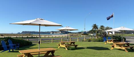 A grassy area with picnic tables and umbrellas, a flag, and a road with directional signs.