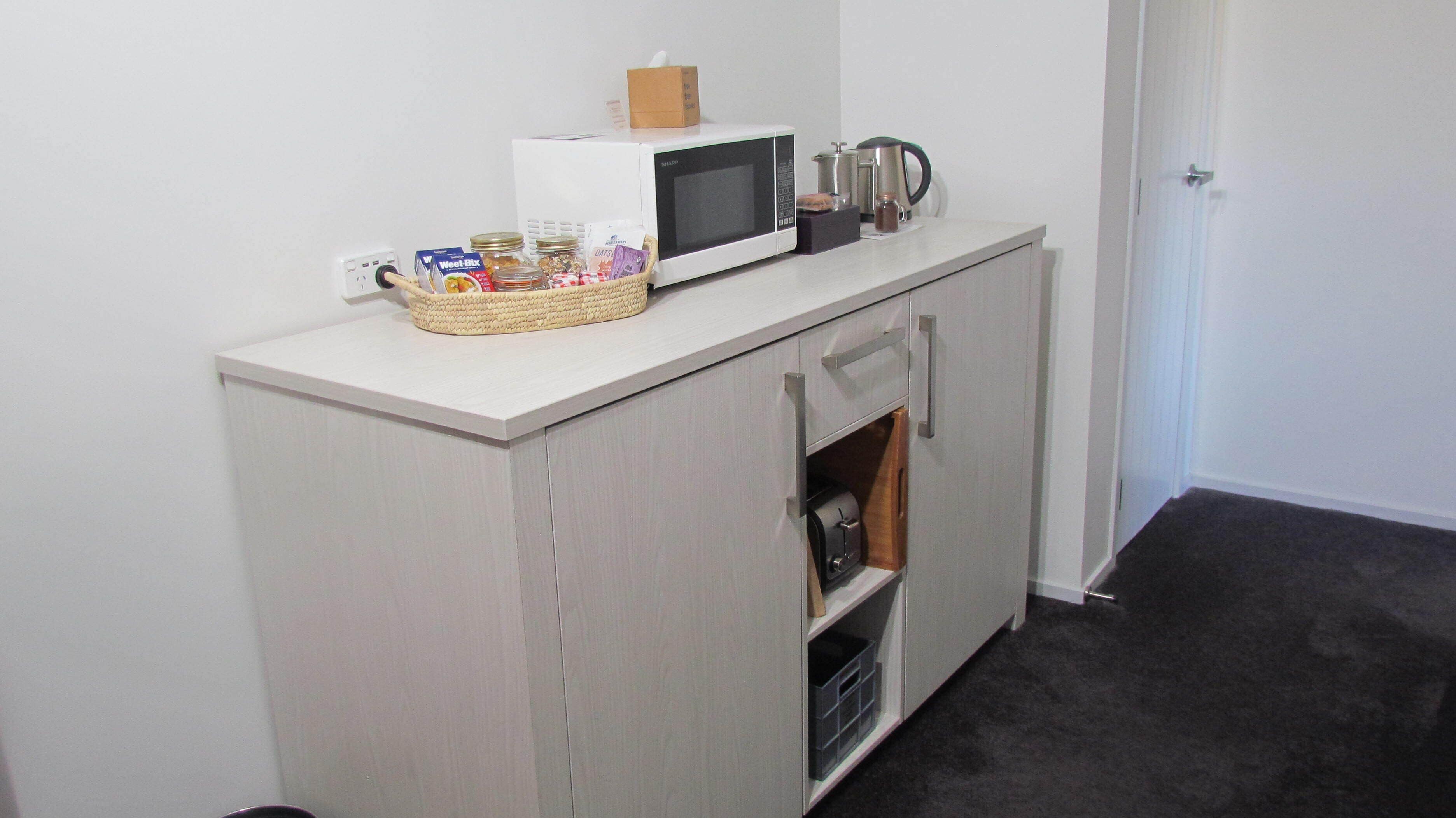 A kitchenette with a microwave, kettle, and storage for snacks and drinks.