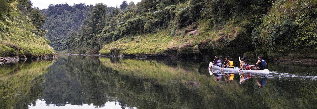 Un groupe de personnes se trouve dans un canoë sur une rivière paisible, entourée d’une végétation luxuriante.