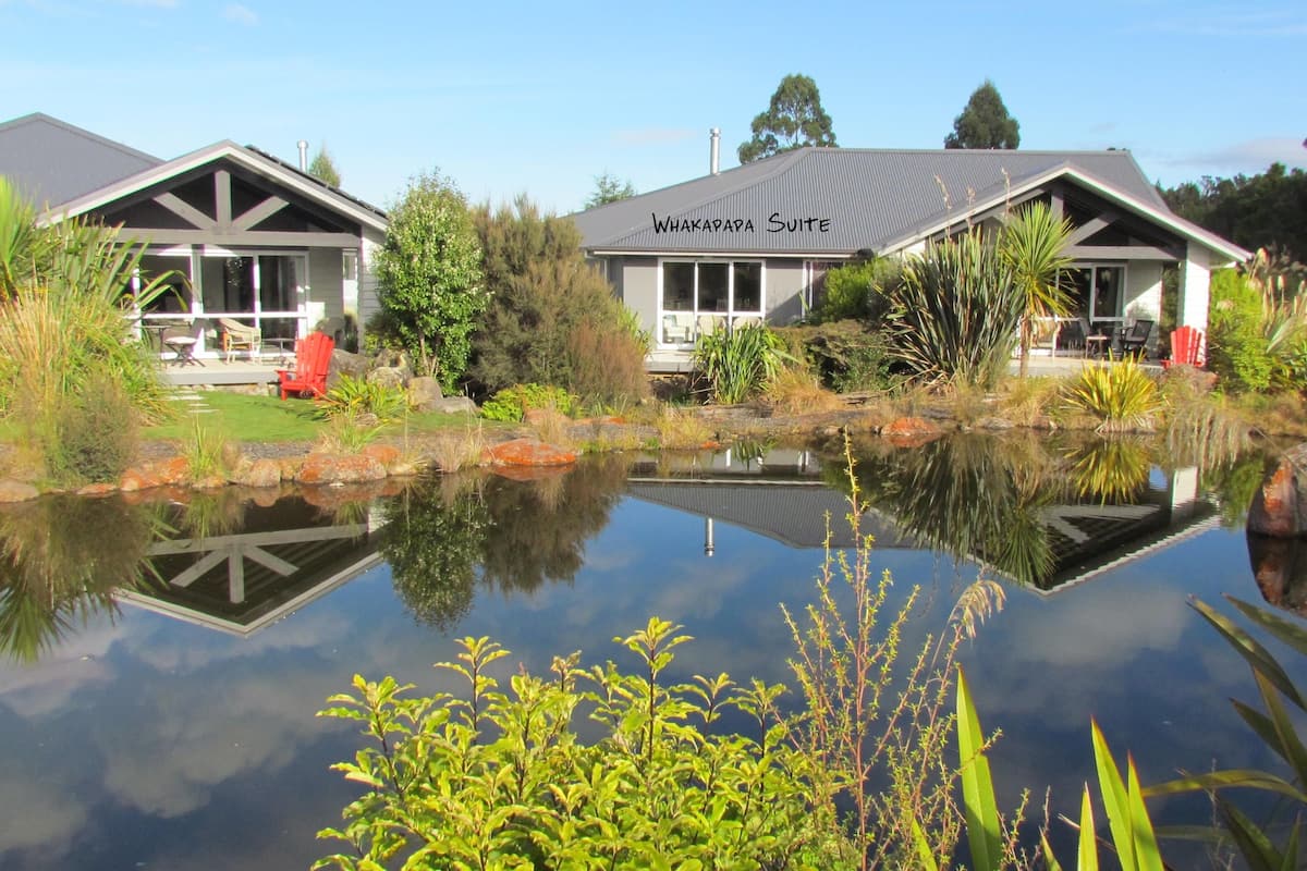 Une suite Whakapapa dotée d’une grande fenêtre, d’un bassin devant et d’un jardin avec différentes espèces de plantes.