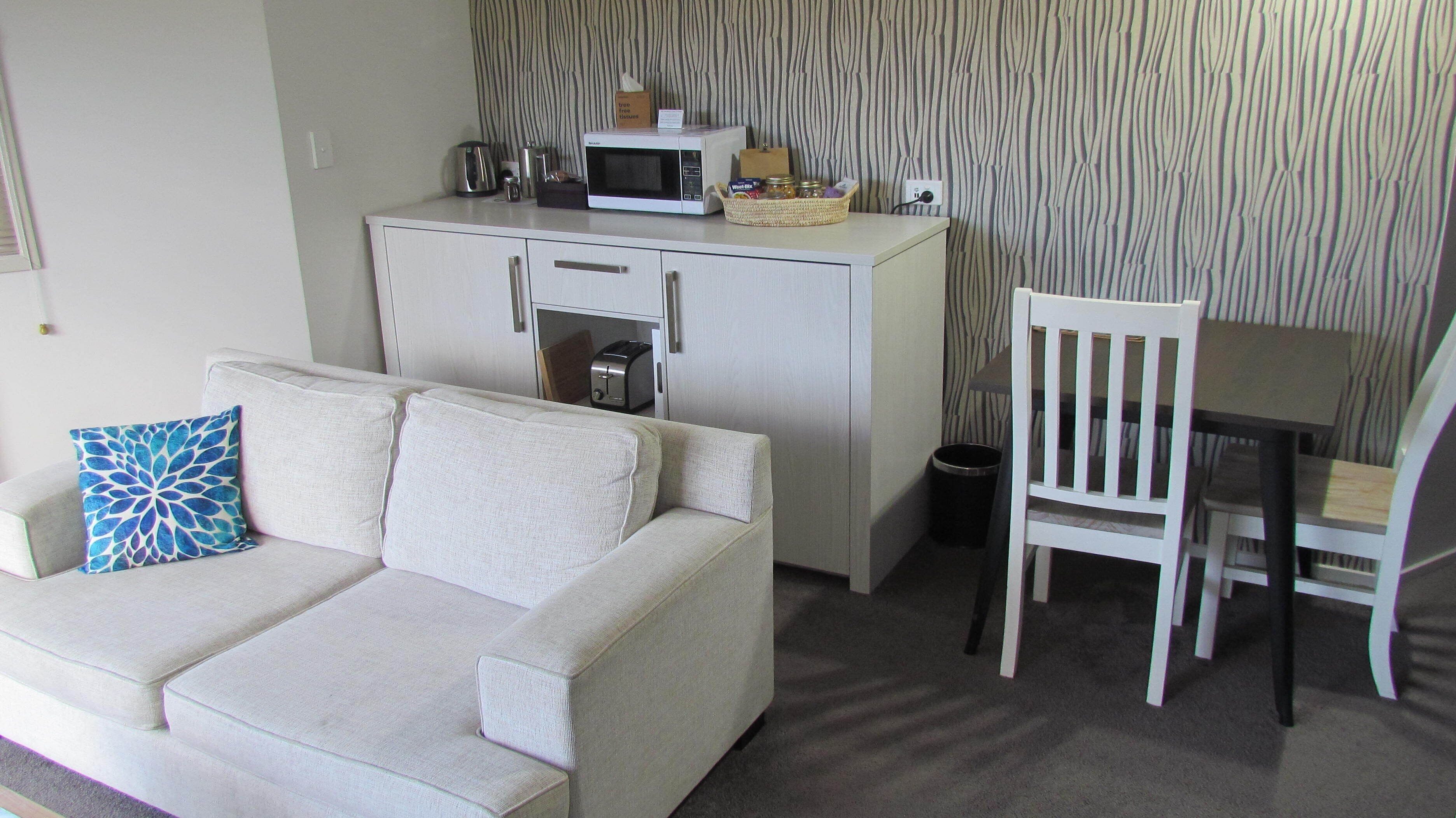 A compact living space with a white sofa, a small table, a microwave, and a trash bin.