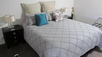 Una cama bien hecha con un diseño acolchado, dos mesitas de noche con lámparas y un estante en la pared.