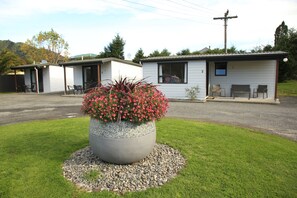 A motel with a large planter of red flowers in front, a gravel driveway, and a grassy area.