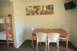Una habitación con literas, una mesa de madera con sillas, un cuadro en la pared y un televisor de pantalla plana montado sobre la mesa.