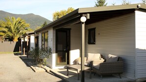 Ein eingeschossiges Mobilheim mit überdachter Terrasse, einer Schiebetür und einer kleinen Sitzgelegenheit im Freien mit Tisch und zwei Stühlen.