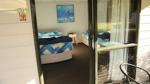 Ein Schlafzimmer mit einem Bett, einem kleinen Nachttisch, einem Stuhl und einem Bild mit einer Strandansicht.