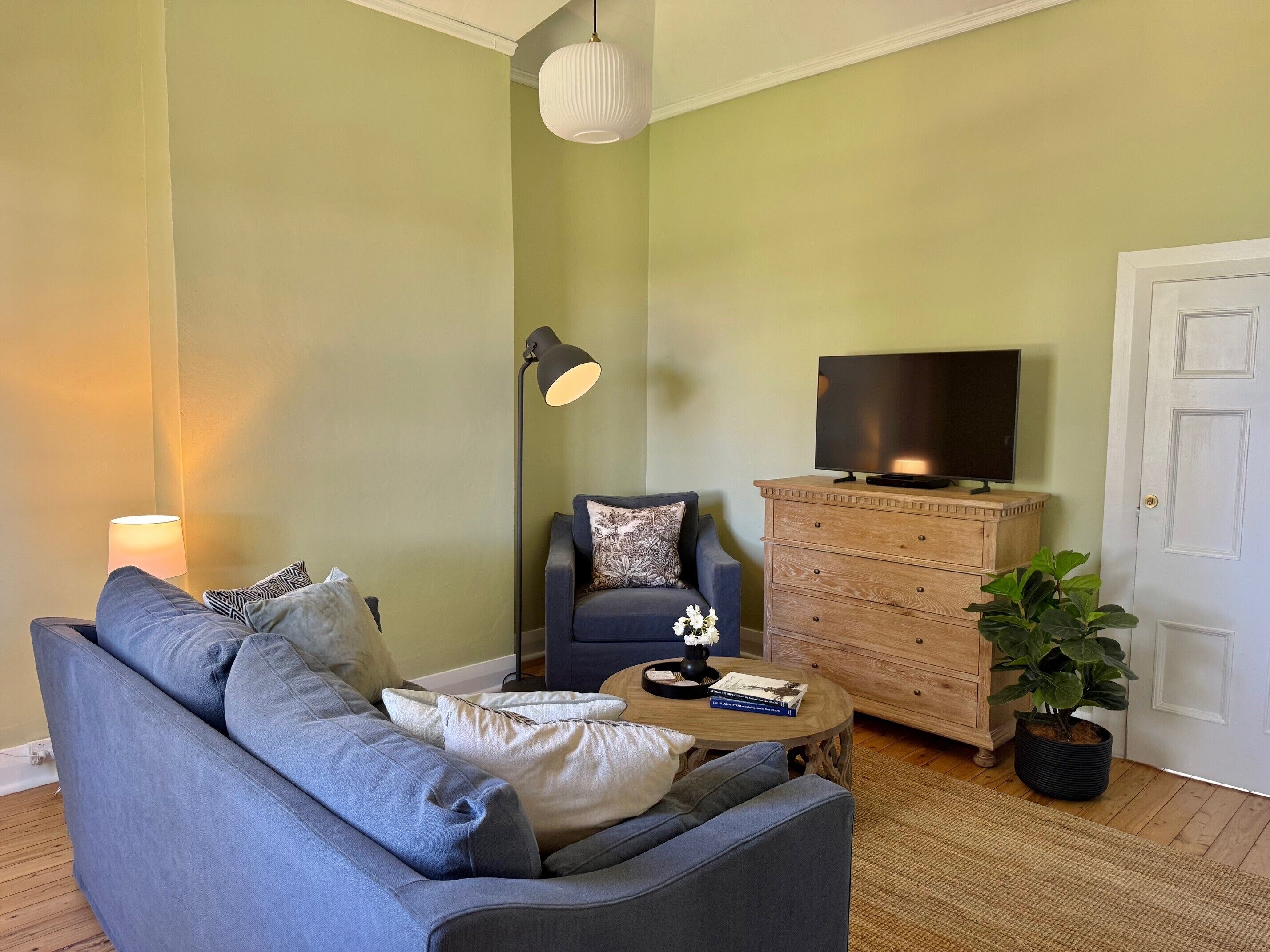 Ein Wohnzimmer mit einer Couch, einem Couchtisch, einem Fernseher auf einer Holzkommode, einer Lampe und einer Topfpflanze.