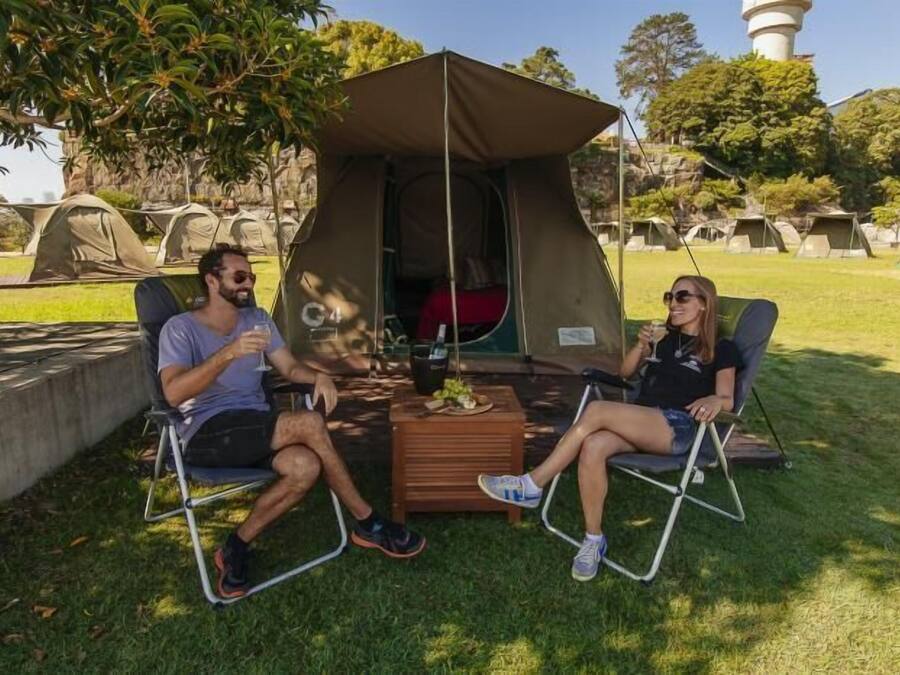 Two people seated at a table under a tent in a camping area with multiple tents in the background.