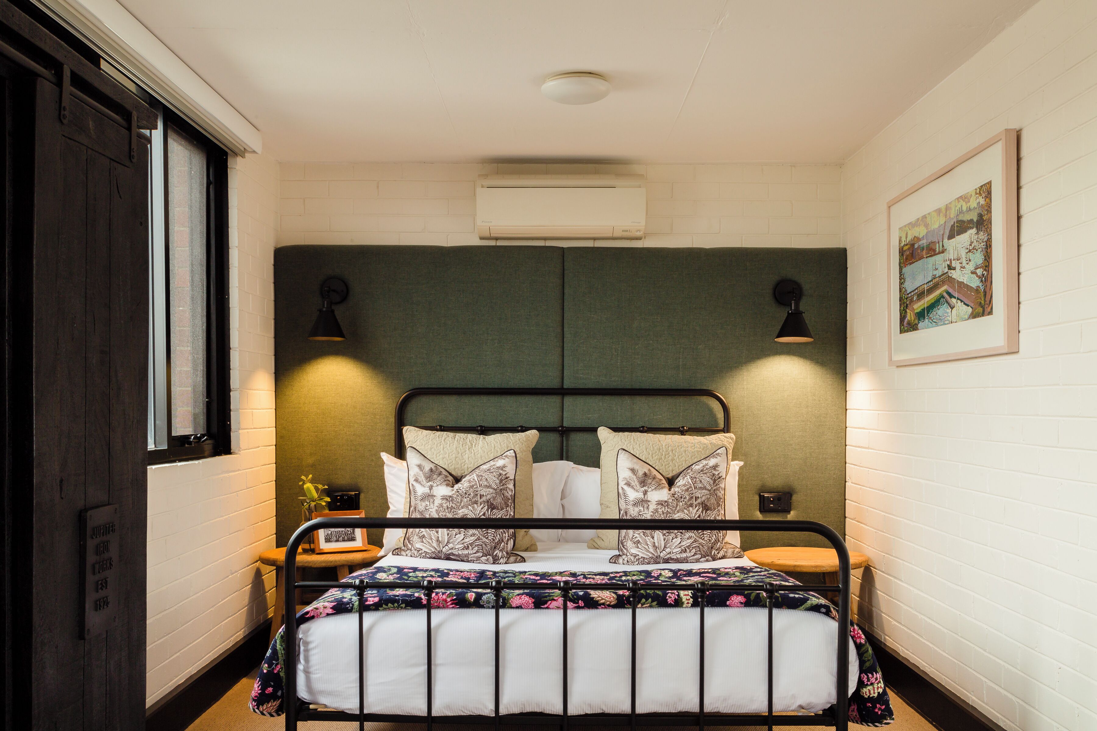 A single bed with a floral bedspread, a headboard, two wall-mounted lamps, and a framed picture on the wall.