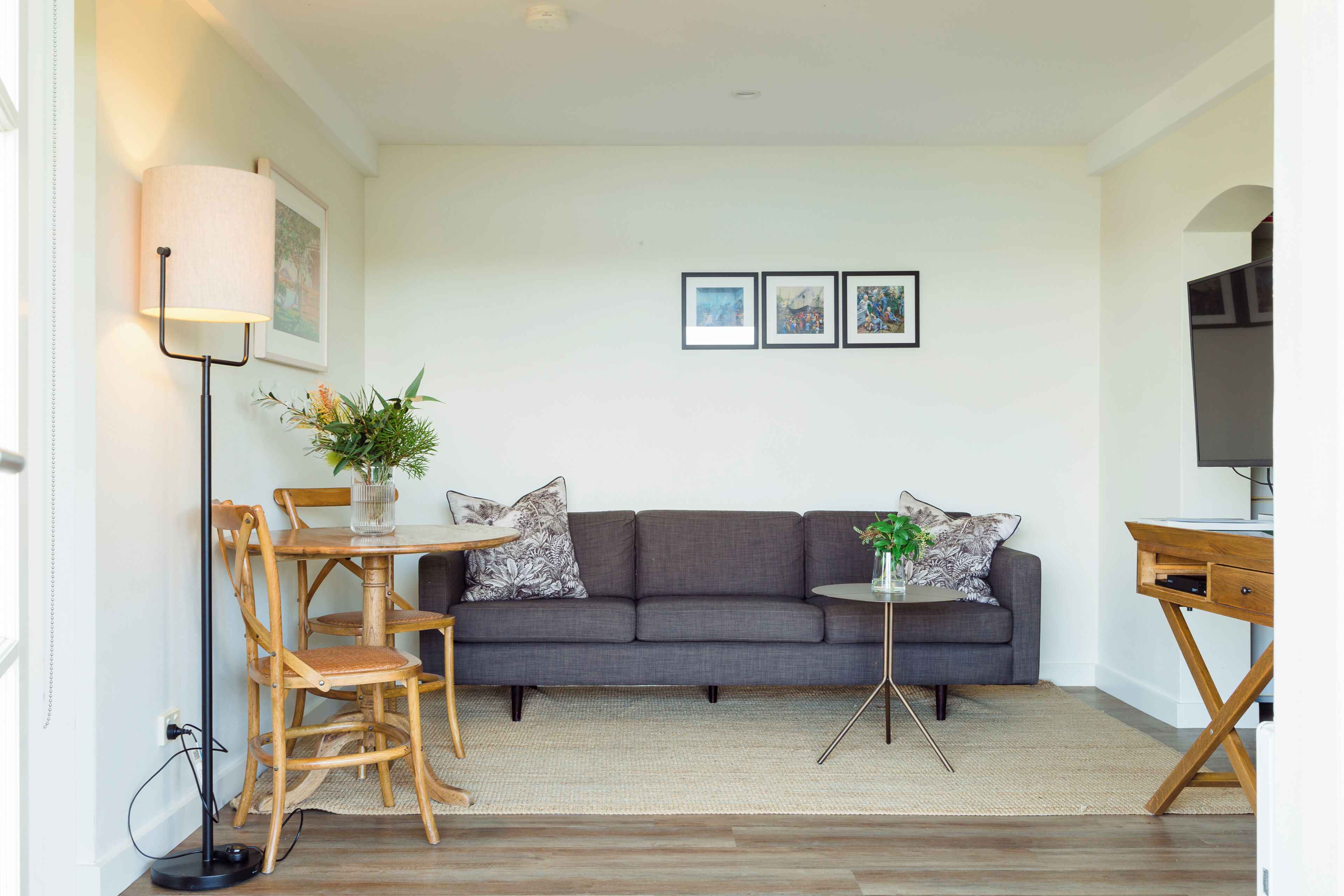 A modern living room with a grey sofa, wooden dining table, and chairs, a floor lamp, and a small side table with a plant.