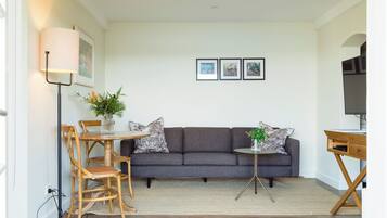 A modern living room with a grey sofa, wooden dining table, and chairs, a floor lamp, and a small side table with a plant.
