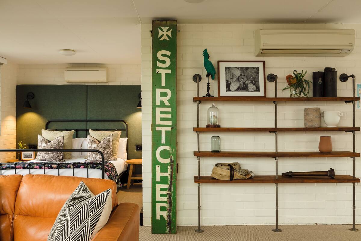 A room with a bed, a green vertical sign, a shelf with various items, and a wall-mounted air conditioner.