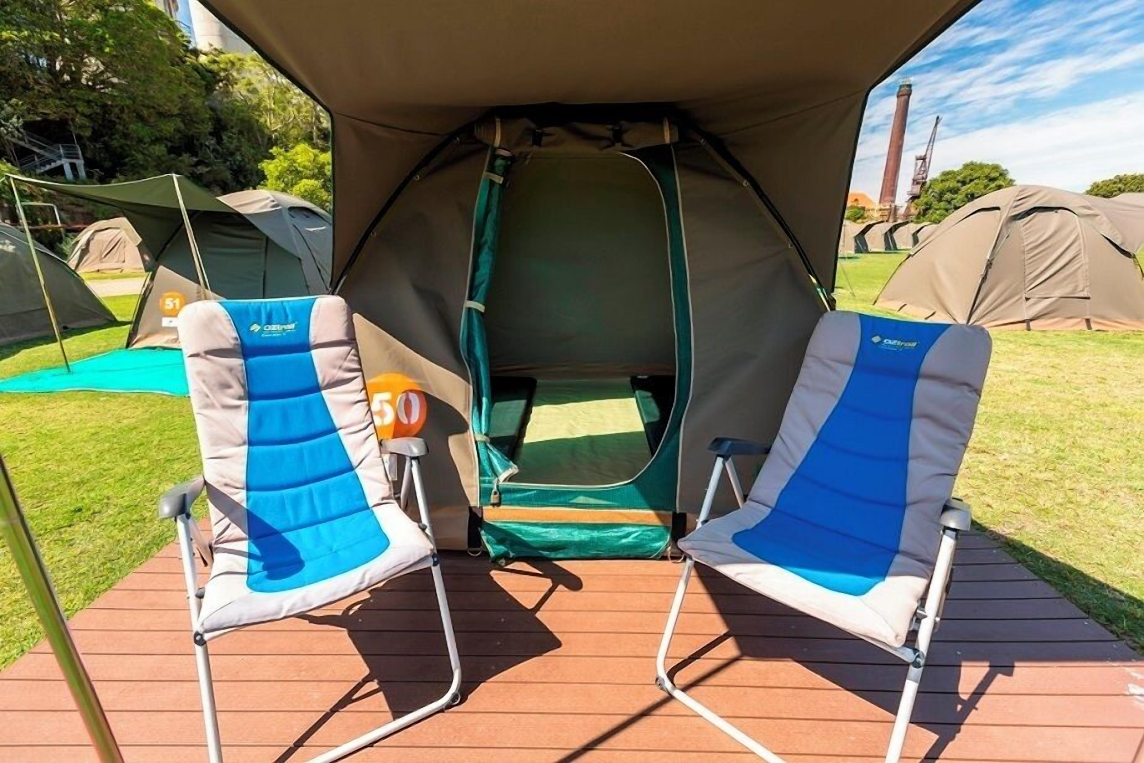 Two camping chairs under a tent with a view of other tents in the background.