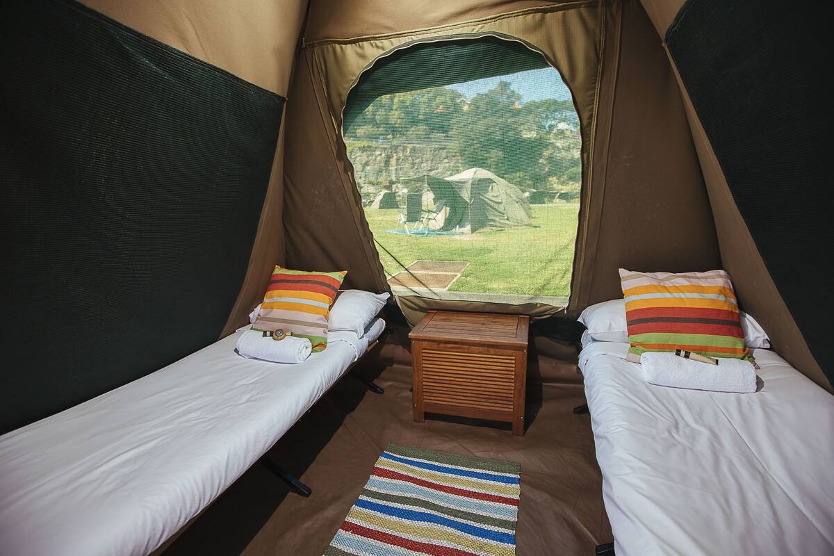 A tent with two beds, each with a pillow and a small wooden table in between.