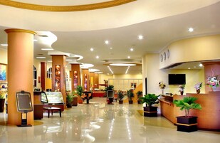 Un hall de hotel con mostrador de recepción, zona de estar y plantas en macetas.