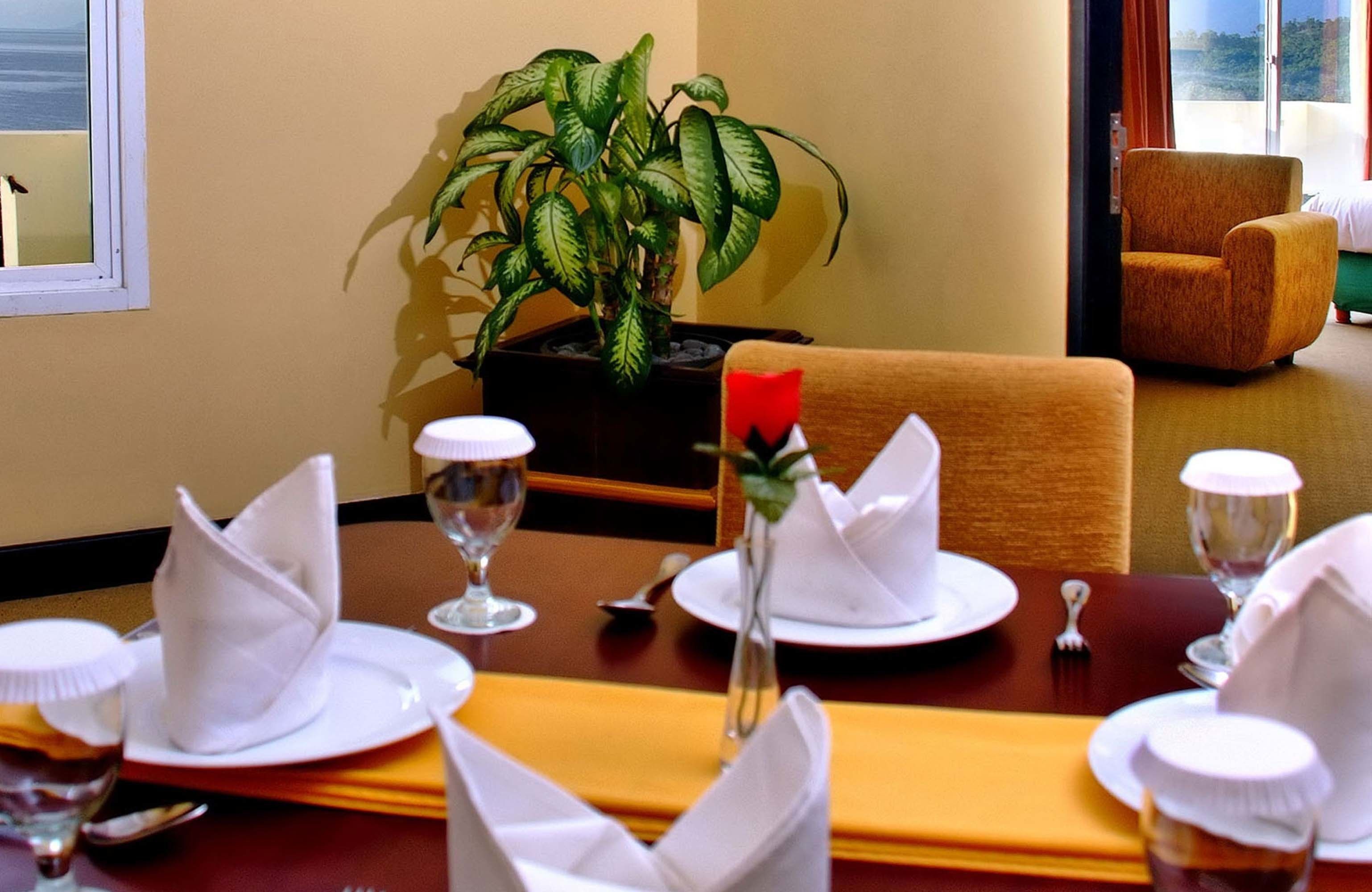 Une table à manger dressée avec des serviettes blanches, des assiettes et des verres à vin, une plante en pot et un bouquet de roses rouges en guise de centre de table.
