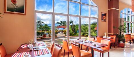 Un restaurante con mesas y sillas, ventanas grandes y vistas al exterior.