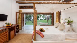 Une chambre avec un lit à baldaquin, une télévision, un bureau avec des fruits et une vue sur l’extérieur.