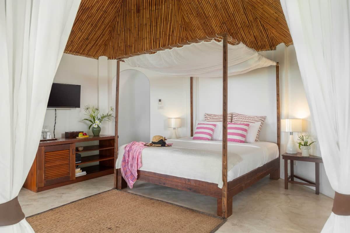 A four-poster bed with a canopy, a television on the wall, a wooden console table, and a bedside table with a lamp.