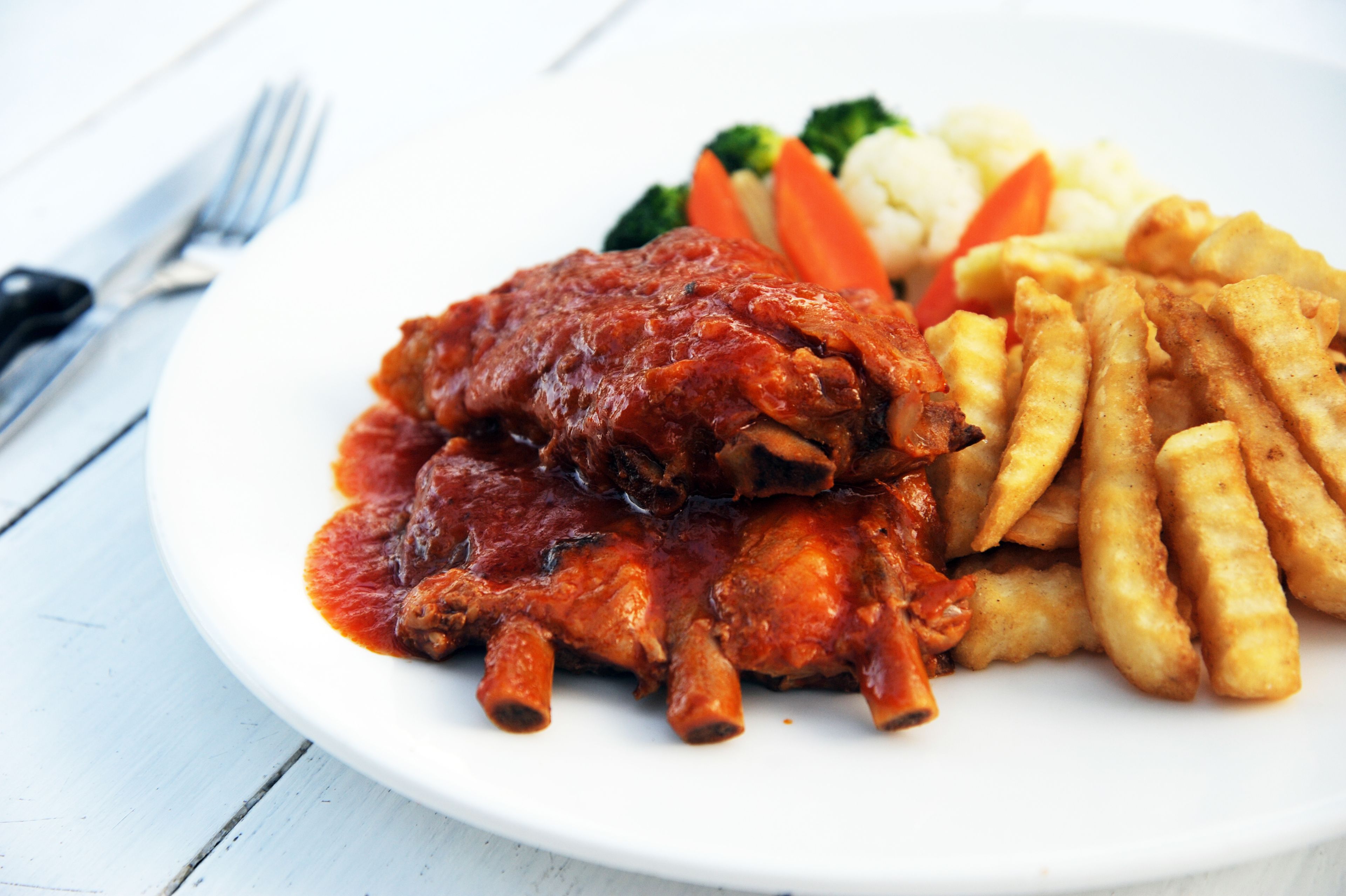 A plate of ribs with sauce, fries, and vegetables.
