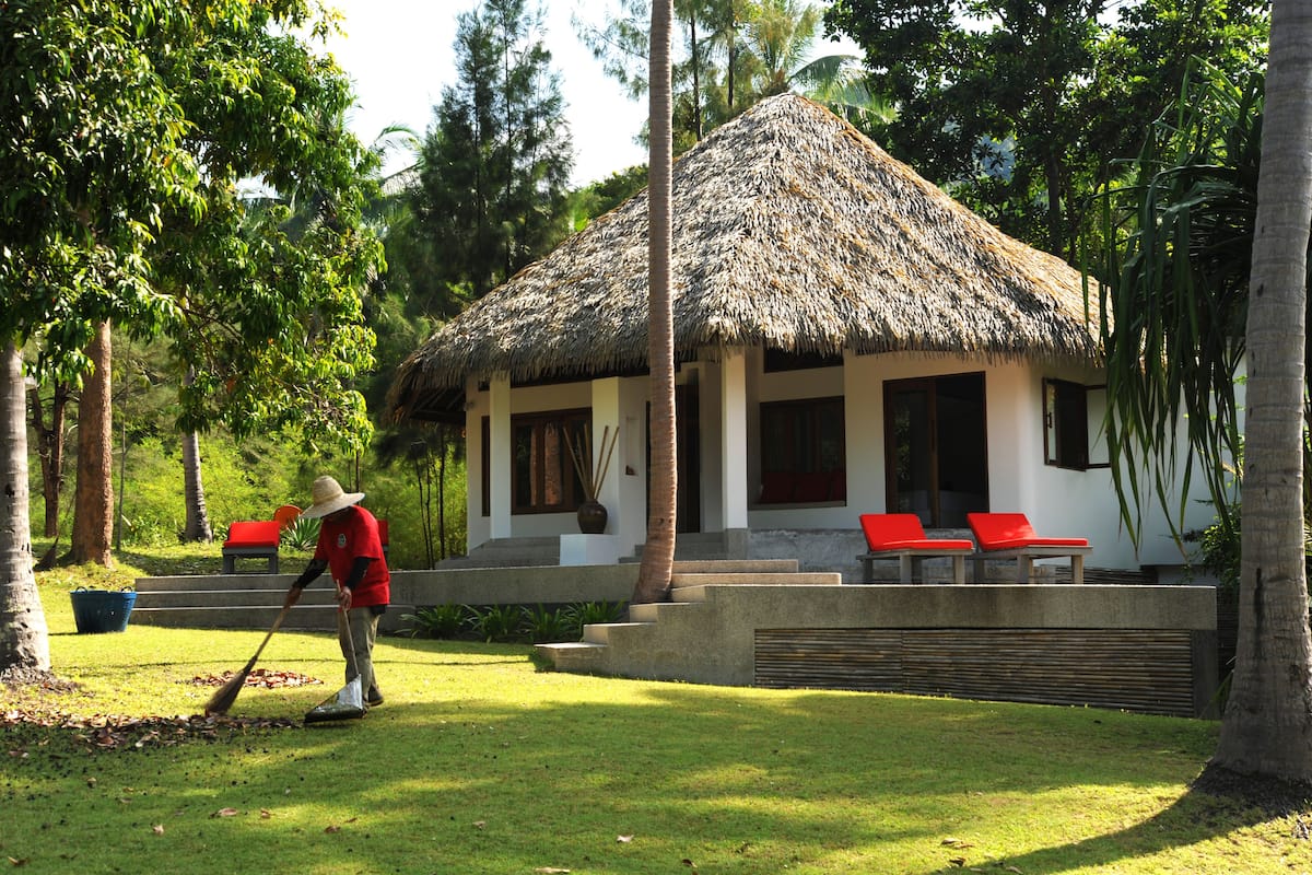 A thatched-roof house with a pool and red lounge chairs.