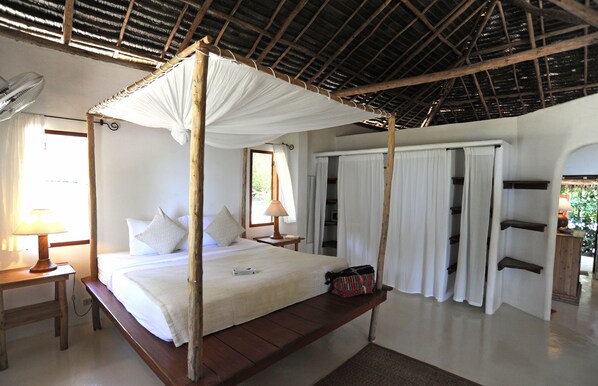 A four-poster bed with a canopy, a bedside table with a lamp, and a bench with a bag.