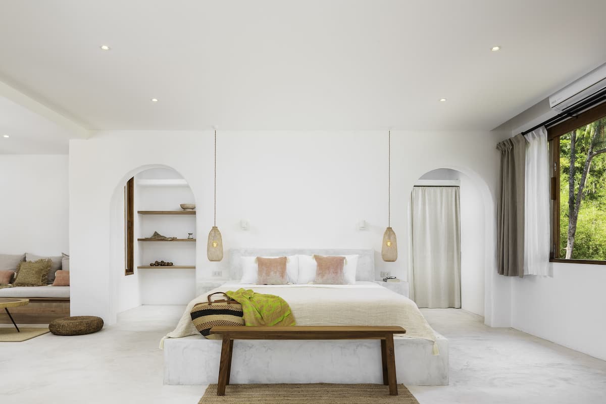A modern bedroom with a large bed, bedside tables, a bench, and a sofa.