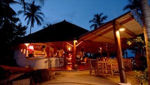 Un bar situé en bord de mer, avec une terrasse, un espace de restauration couvert et une piscine.