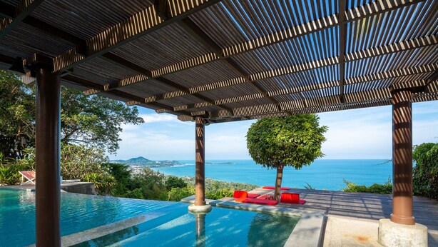 Une piscine à débordement offrant une vue sur la mer, un espace salon couvert et un jardin bien entretenu.