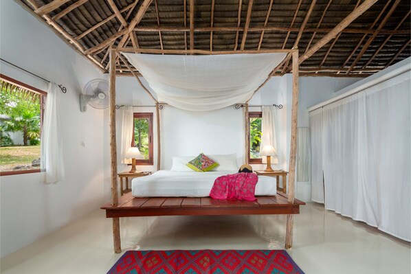 A room with a bed under a wooden canopy, white walls, and a view of greenery outside. - The Jungle Club (Koh Samui)