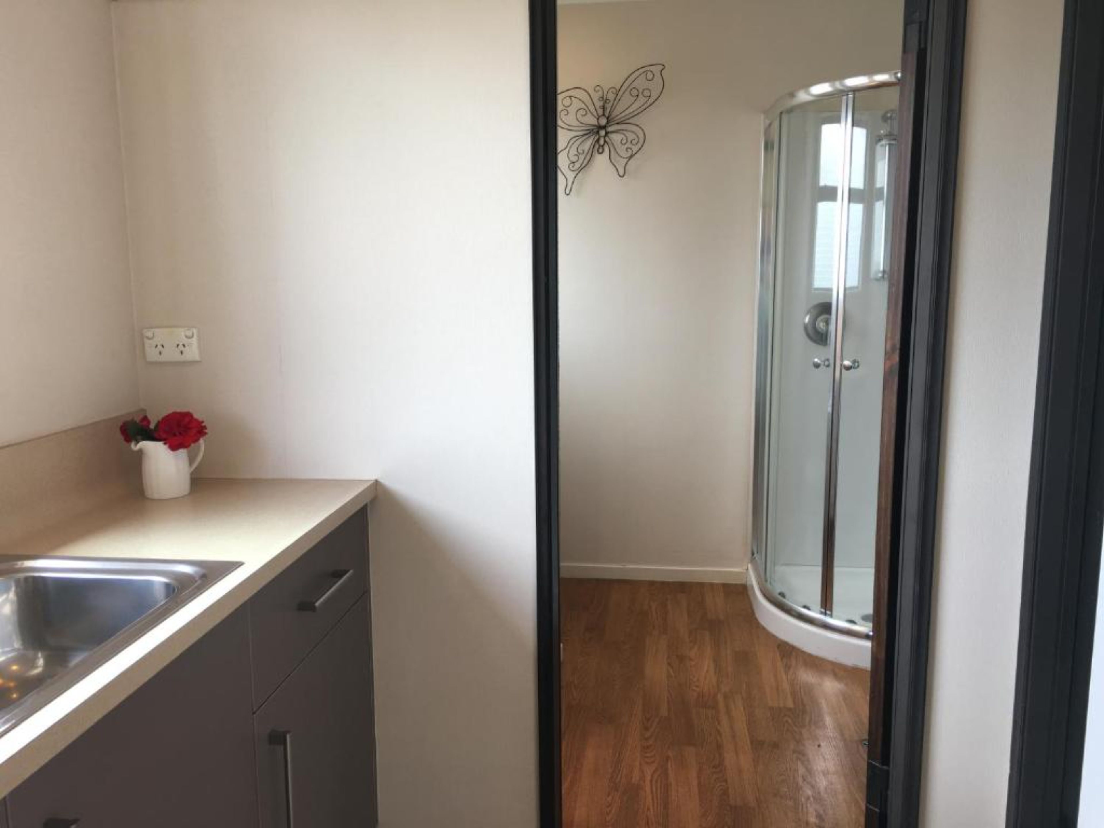 Een moderne badkamer met een glazen douchecabine, een witte wastafel en een vaas met rode bloemen op het aanrecht.
