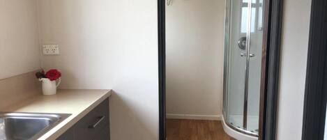 Een moderne badkamer met een glazen douchecabine, een witte wastafel en een vaas met rode bloemen op het aanrecht.