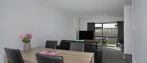 A modern room with a dining table, chairs, a TV, and a sofa.