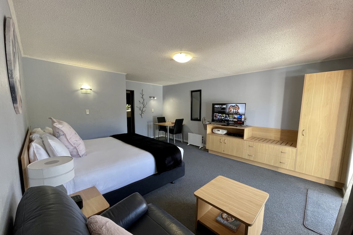 Una habitación de hotel con cama, sofá, mueble de madera, televisión y escritorio.