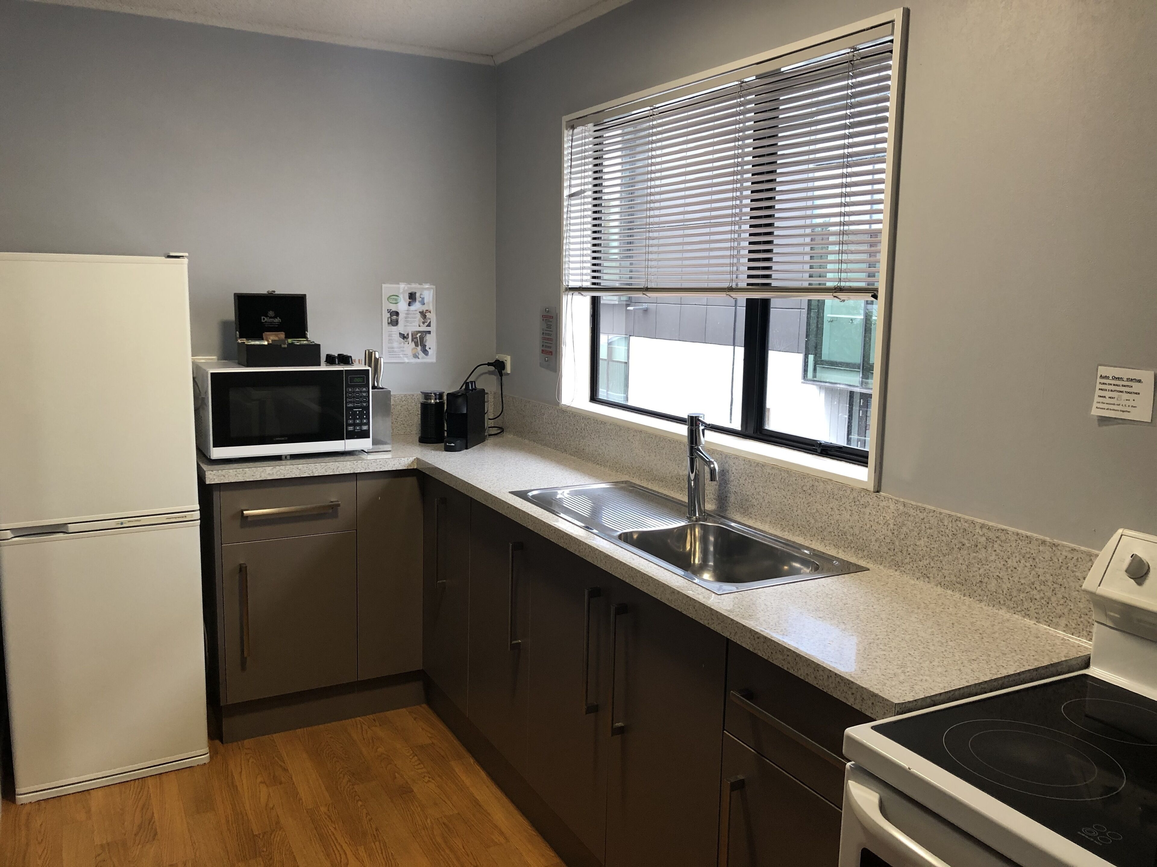 A compact kitchen with a refrigerator, microwave, coffee maker, sink, and stove.